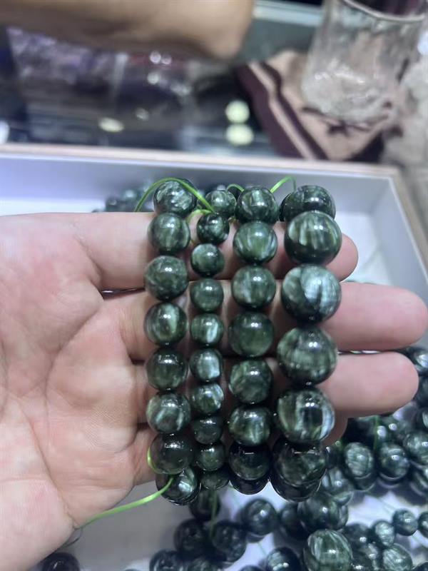 Seraphinite bead strands held in hand during a size and finish check